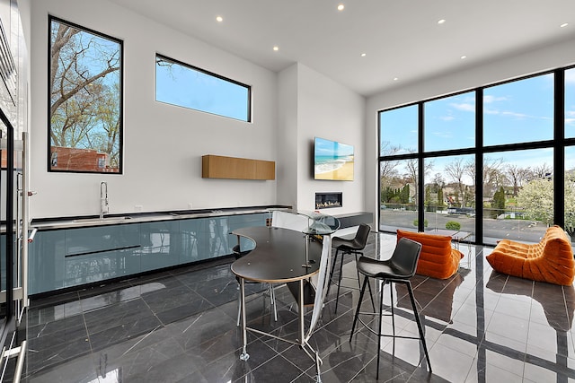 dining space featuring a towering ceiling, recessed lighting, healthy amount of natural light, and a glass covered fireplace
