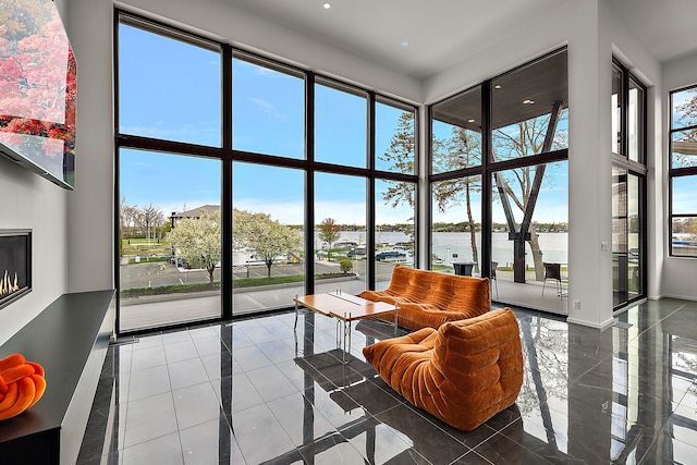 sunroom / solarium featuring a water view, healthy amount of natural light, a towering ceiling, recessed lighting, and tile patterned floors