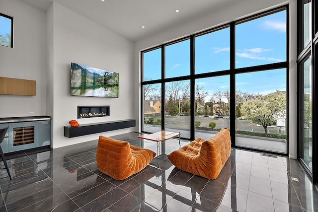 living area with a towering ceiling, a glass covered fireplace, healthy amount of natural light, and recessed lighting