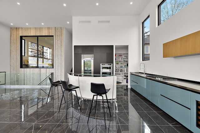 kitchen with modern cabinets, a sink, dark countertops, a towering ceiling, and recessed lighting