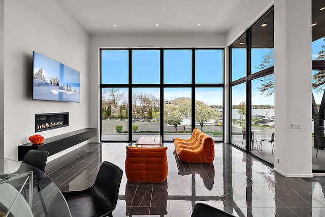 living room with a towering ceiling, plenty of natural light, a glass covered fireplace, and recessed lighting