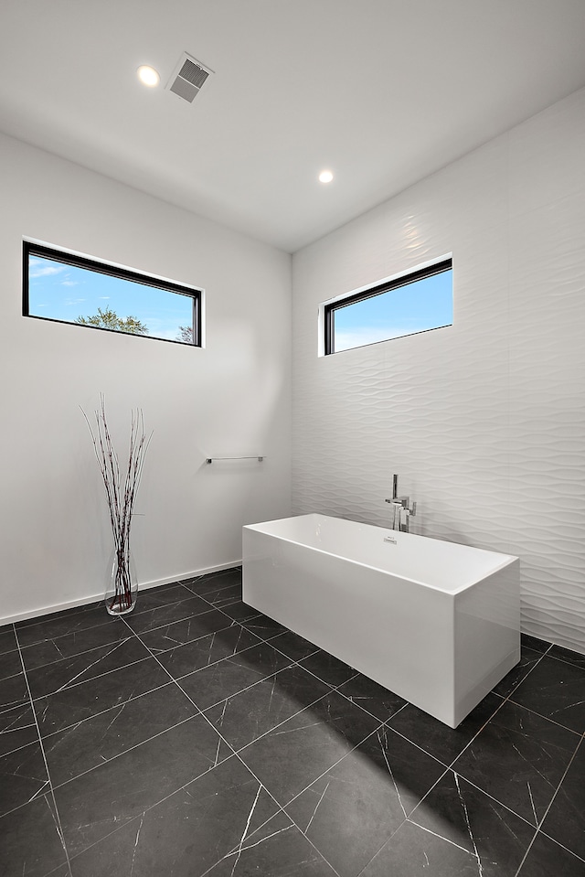 bathroom featuring a freestanding tub, marble look tiles, and recessed lighting