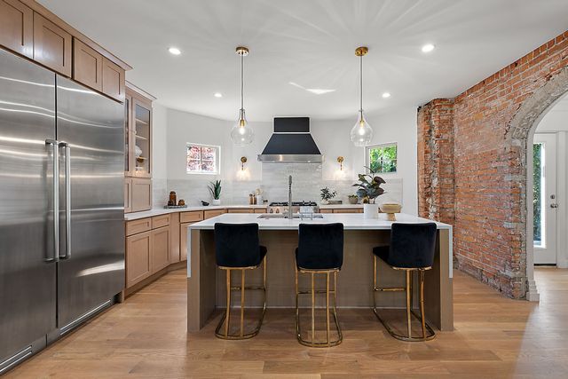 2423 Chicago Blvd, Detroit, MI 48206 - kitchen featuring wall chimney range hood, arched walkways, brick wall, stainless steel built in fridge, and backsplash