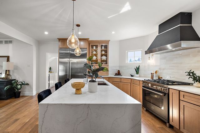 2423 Chicago Blvd, Detroit, MI 48206 - kitchen featuring an island with sink, decorative backsplash, light wood-style floors, high quality appliances, and wall chimney range hood