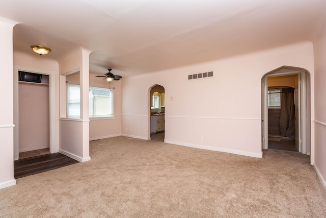 unfurnished living room with a ceiling fan, visible vents, arched walkways, carpet floors, and baseboards