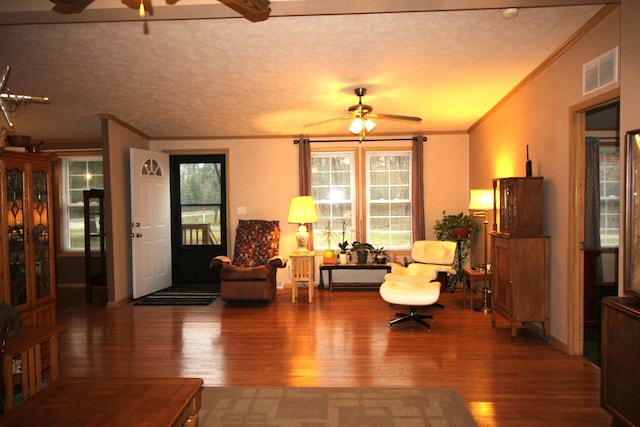 living area with ornamental molding, a ceiling fan, visible vents, and wood finished floors
