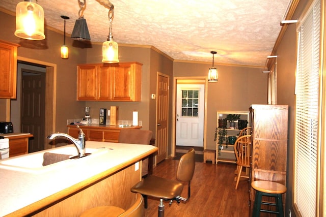 kitchen with a sink, light countertops, ornamental molding, dark wood finished floors, and decorative light fixtures