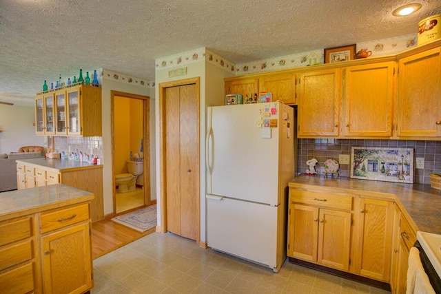 1414 Plains Rd, Leslie, MI 49251 - kitchen featuring a textured ceiling, decorative backsplash, glass insert cabinets, freestanding refrigerator, and light floors