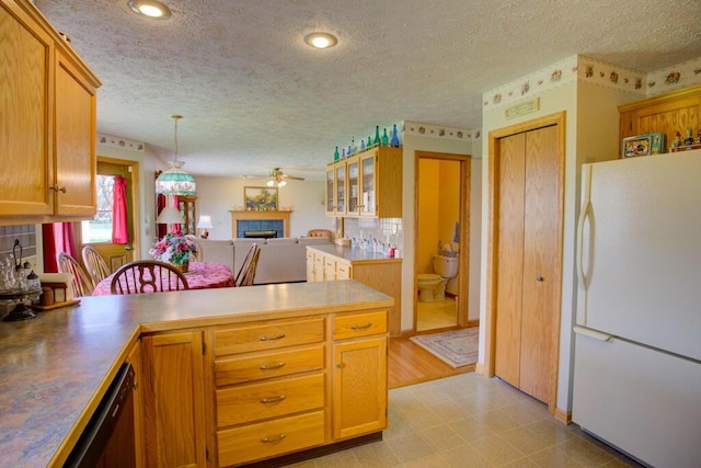 1414 Plains Rd, Leslie, MI 49251 - kitchen featuring freestanding refrigerator, a textured ceiling, ceiling fan, a fireplace, and a peninsula