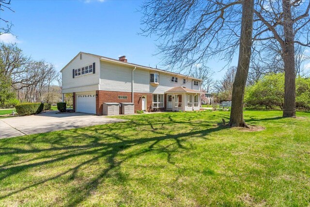 view of front facade featuring a chimney, driveway, brick siding, a garage, and a front yard