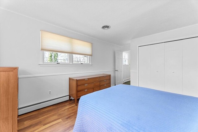 bedroom featuring multiple windows, visible vents, baseboard heating, and wood finished floors