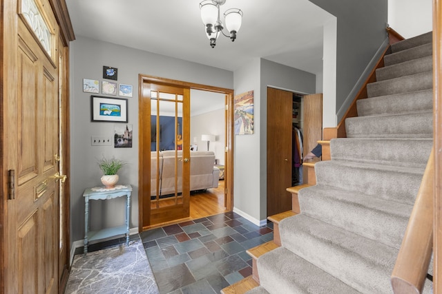 entryway with an inviting chandelier, stairway, stone finish floor, and baseboards