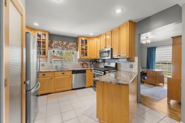 kitchen featuring light tile patterned floors, a sink, appliances with stainless steel finishes, plenty of natural light, and a peninsula
