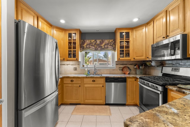 kitchen with a sink, appliances with stainless steel finishes, light tile patterned flooring, light stone countertops, and backsplash