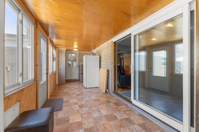 unfurnished sunroom with stone finish flooring, wood walls, brick wall, and wood ceiling