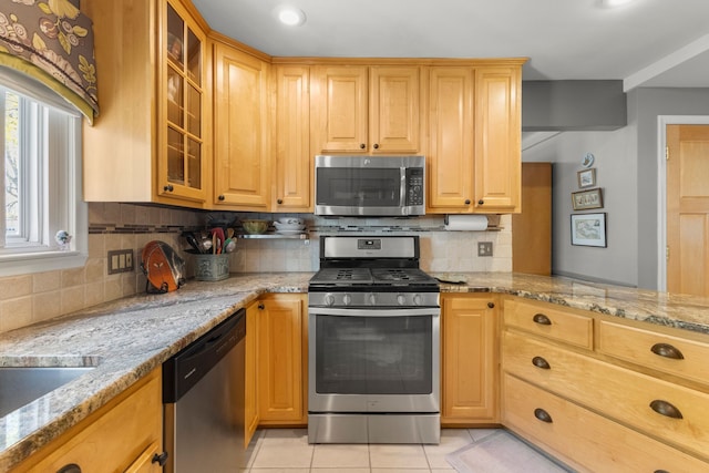 kitchen with appliances with stainless steel finishes, light tile patterned floors, tasteful backsplash, and light stone countertops