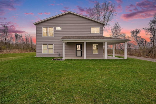 back of property at dusk featuring driveway and a yard