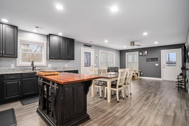 kitchen with visible vents, light wood-style floors, butcher block counters, a ceiling fan, and dark cabinetry