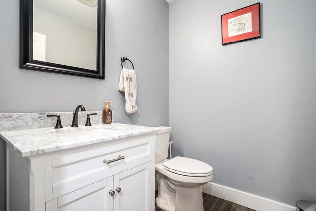 bathroom with toilet, vanity, wood finished floors, and baseboards