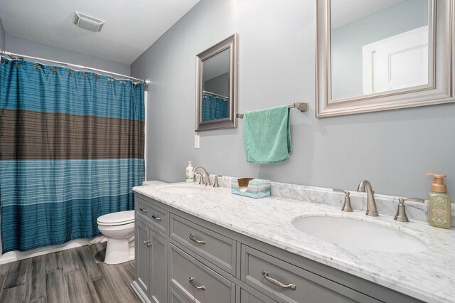 full bath featuring toilet, a sink, wood finished floors, and visible vents