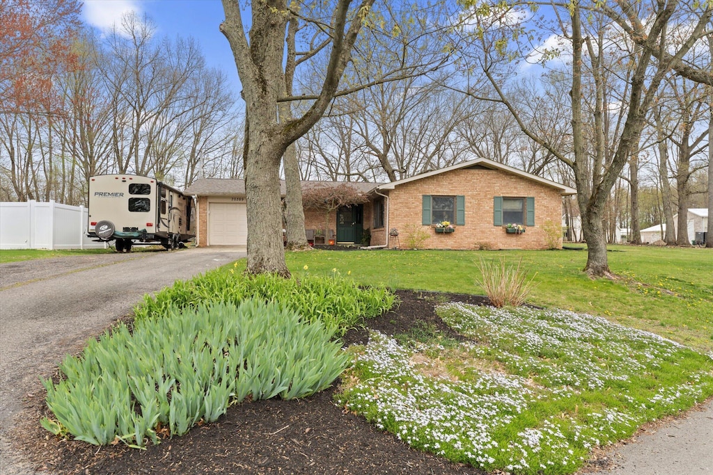 view of front of home with brick siding, fence, a garage, driveway, and a front lawn
