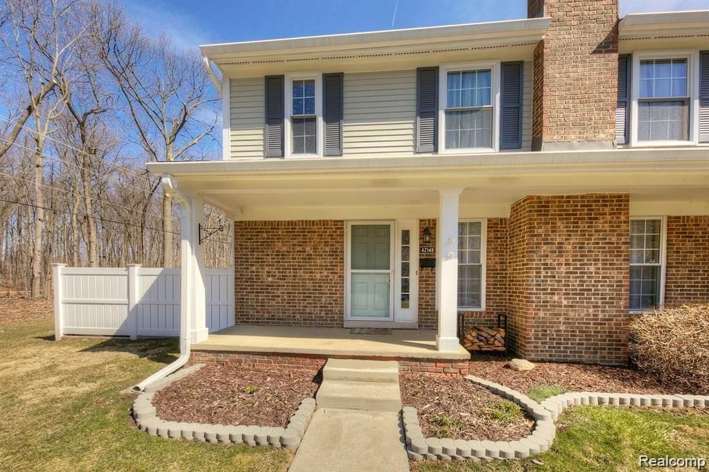 doorway to property with a chimney, brick siding, a porch, and fence