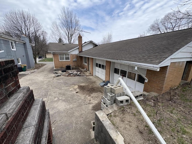 back of house with concrete driveway, a chimney, a shingled roof, brick siding, and a garage