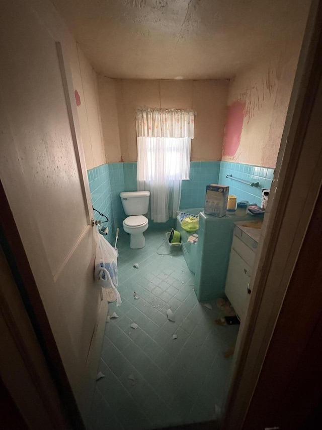 bathroom featuring toilet, a wainscoted wall, and tile walls