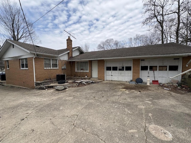 exterior space featuring a chimney, brick siding, central air condition unit, a garage, and concrete driveway