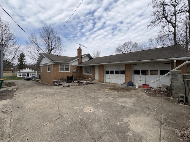 exterior space featuring concrete driveway, a chimney, a shingled roof, an attached garage, and brick siding