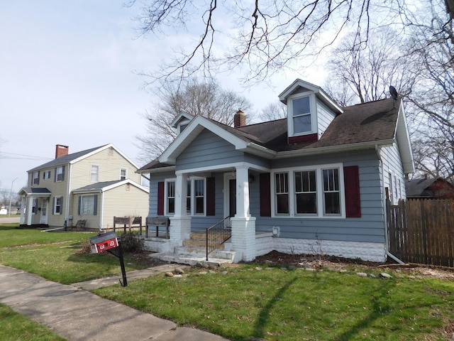 view of front of home featuring a porch, fence, a chimney, and a front yard