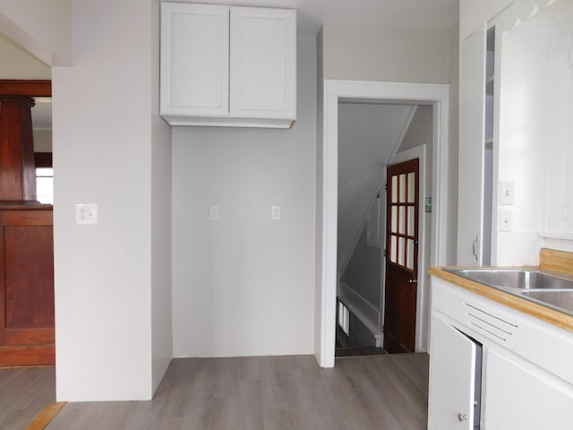 kitchen with light wood-type flooring, light countertops, white cabinets, and a sink