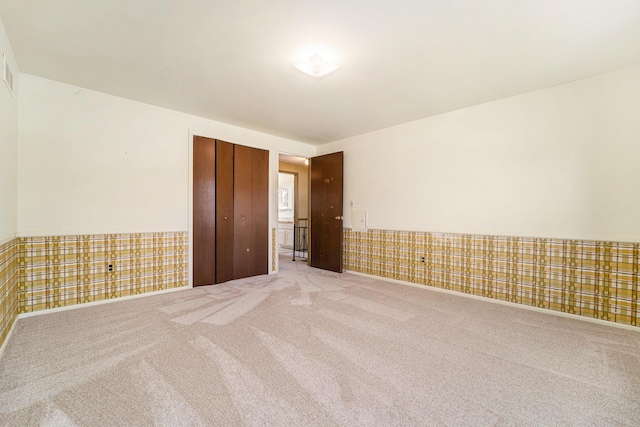 carpeted spare room with visible vents, a wainscoted wall, and wallpapered walls