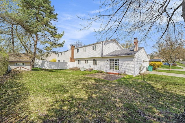 rear view of property with a chimney, concrete driveway, fence, and a yard