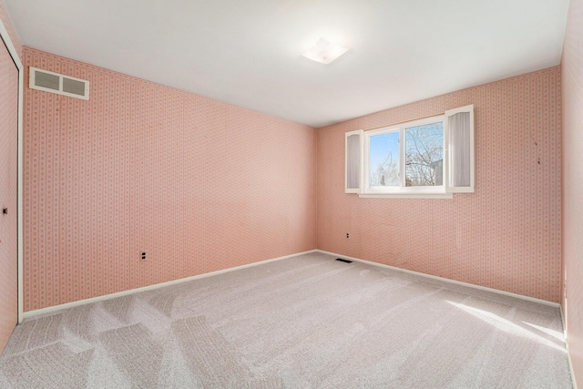 spare room featuring carpet, visible vents, and wallpapered walls