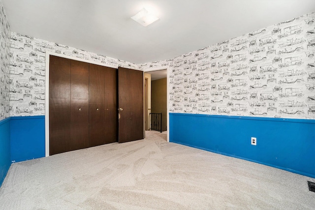 unfurnished bedroom with a wainscoted wall, a closet, carpet flooring, and wallpapered walls