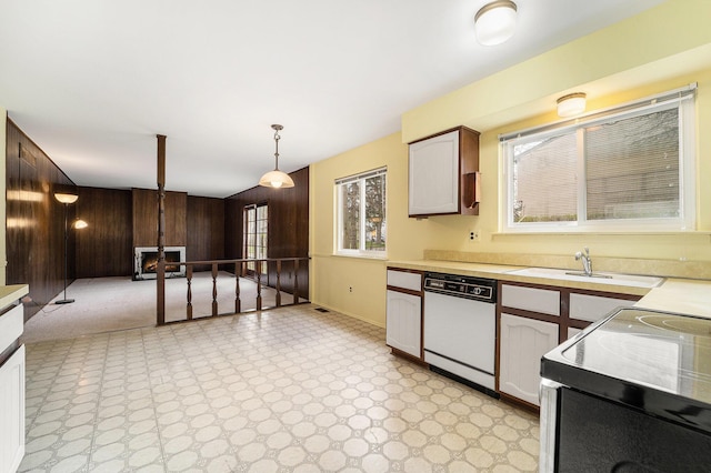 kitchen with light countertops, wood walls, electric range oven, dishwasher, and a sink