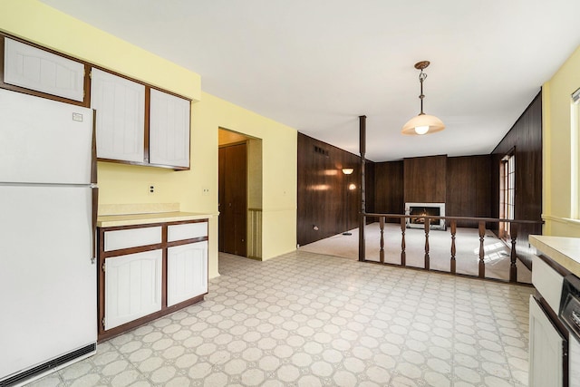 kitchen with wood walls, a warm lit fireplace, light countertops, and freestanding refrigerator