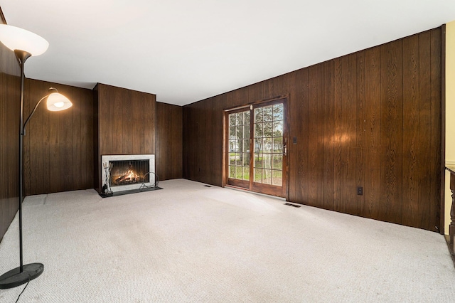 unfurnished living room with a fireplace with flush hearth, wooden walls, visible vents, and light carpet