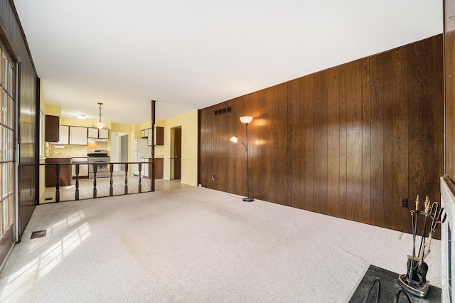 unfurnished living room featuring visible vents, light carpet, and wooden walls