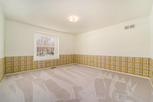 carpeted spare room with visible vents and wainscoting