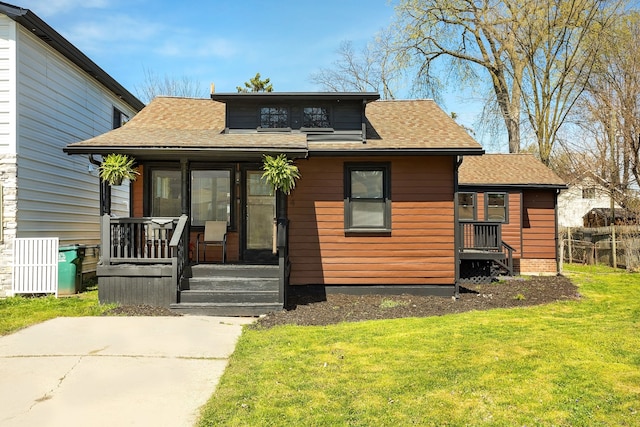 view of front of house featuring roof with shingles, covered porch, and a front lawn