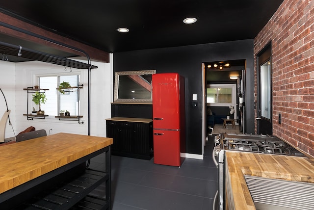 kitchen with wood counters, stainless steel gas range oven, dark tile patterned floors, and brick wall