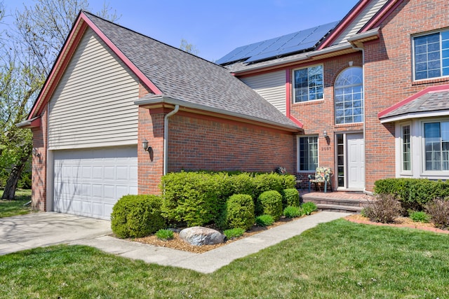 traditional-style home featuring a shingled roof, brick siding, a front yard, roof mounted solar panels, and driveway