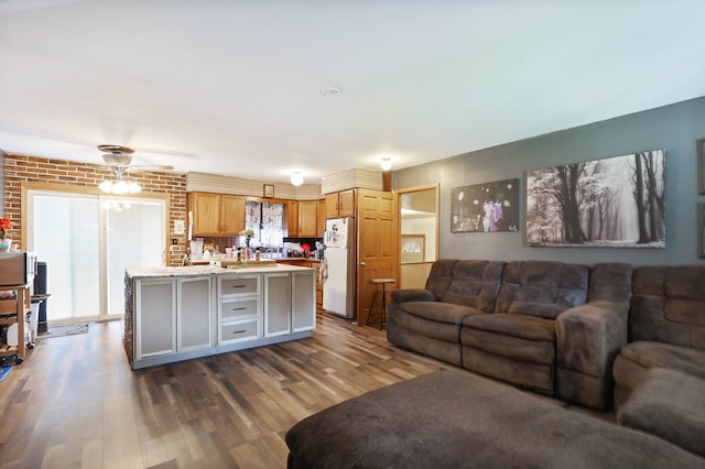 living area featuring a ceiling fan, brick wall, and dark wood finished floors