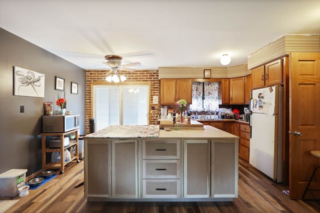 kitchen with stainless steel microwave, freestanding refrigerator, brown cabinetry, ceiling fan, and dark wood-style flooring
