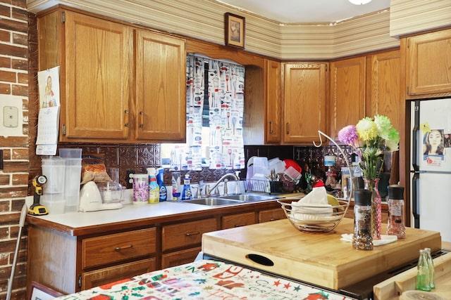 kitchen featuring brown cabinets, a sink, tasteful backsplash, light countertops, and freestanding refrigerator