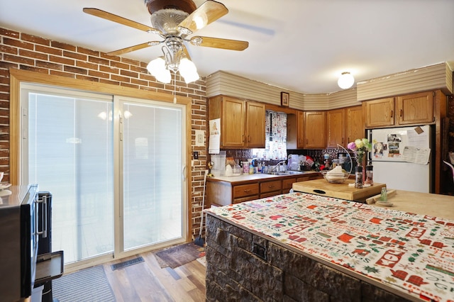kitchen featuring freestanding refrigerator, brown cabinetry, light wood-style floors, light countertops, and a ceiling fan