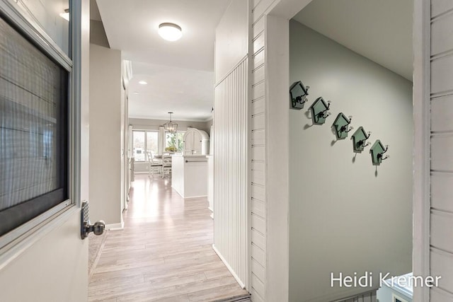 hall featuring baseboards, a notable chandelier, and light wood-style floors