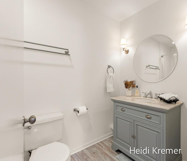 bathroom with toilet, vanity, wood finished floors, and baseboards